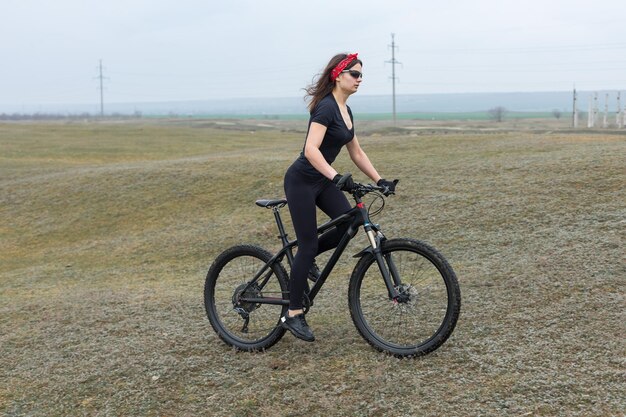 Meisje op een mountainbike op offroad mooi portret van een fietser in regenachtig weer Fitness meisje rijdt op een moderne koolstofvezel mountainbike in sportkleding Close-up portret van een meisje in rode bandana