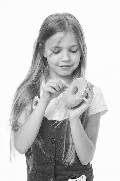 Meisje op lachend gezicht houdt zoete donut in de hand geïsoleerd op witte achtergrond Kid meisje met lang haar houdt van snoep en lekkernijen Zoete tand concept Meisje eet graag donuts met kleurrijke toppings