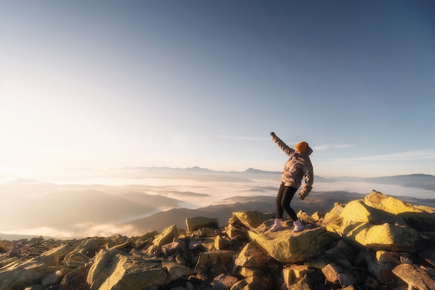 Meisje op rotsachtige bergpiek kijken naar prachtige bergvallei in mist bij zonsondergang