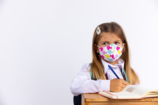 Meisje op school walging het dragen van een beschermend masker zittend in de tafel bij les. Nieuwe normale schoolregels, gezondheids- en epidemisch concept.