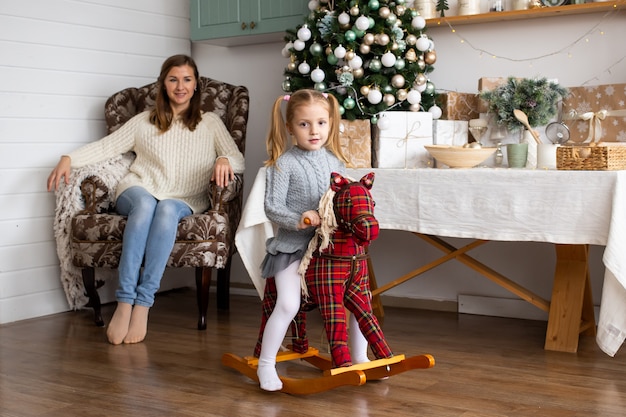 Meisje op speelgoed paard en haar moeder in kerstkeuken thuis.