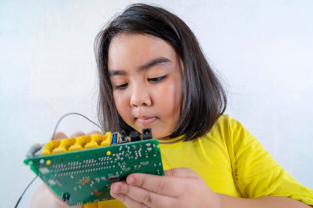 Meisje op zoek naar printplaat door vergrootglas op de houten tafel thuis en bouwt een robot als een wetenschappelijk schoolproject