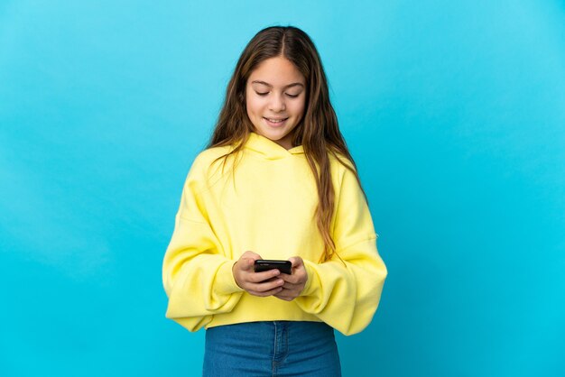 Meisje over geïsoleerd blauw dat een bericht met mobiel verzendt