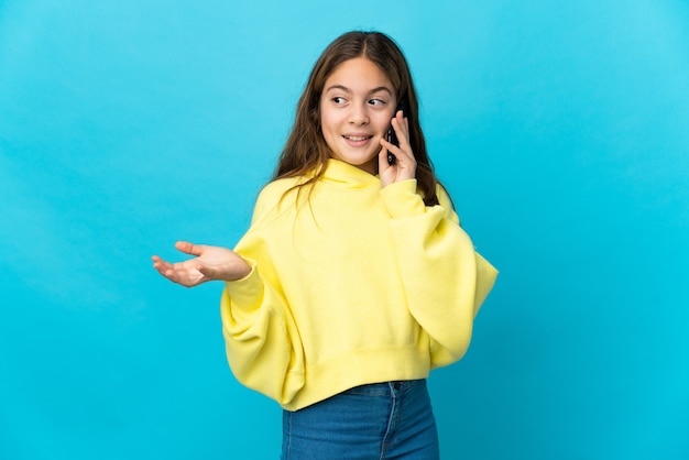 Meisje over geïsoleerde blauwe achtergrond die een gesprek met de mobiele telefoon met iemand houdt