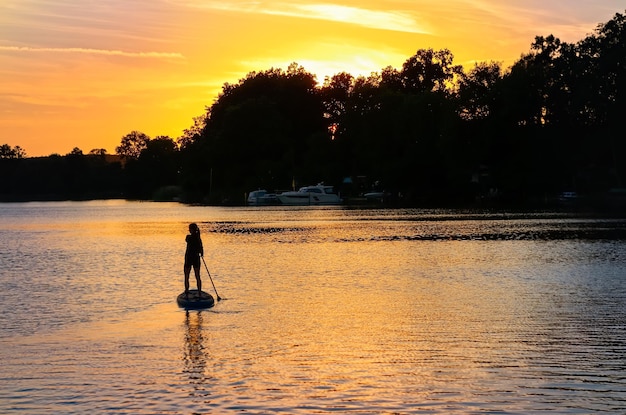 Meisje peddelen op SUP board op prachtig meer tijdens zonsondergang of zonsopgang, opstaan paddle boarding