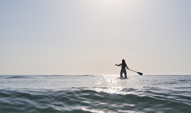 Meisje peddelend op een paddleboard bij zonsopgang