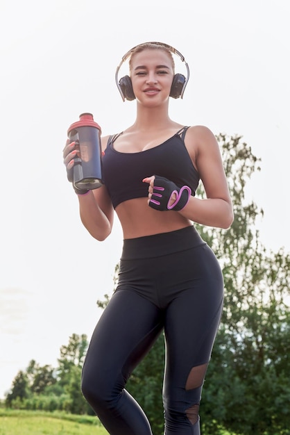 Meisje poseren met een sportvoeding shaker in het park Het concept van een gezonde levensstijl Sportuitrusting Fitness stijl advertentie