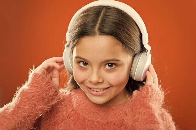 Meisje schattig klein kind draagt koptelefoon luister muziek Kind luister muziek oranje achtergrond Aanbevolen muziek op basis van aanvankelijke interesse Vertel me waar je naar luistert en ik zal je vertellen wie je bent