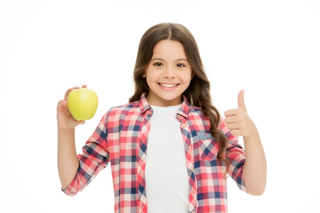 Meisje schattig lang krullend haar houdt appel fruit witte achtergrond Kind meisje casual kleding houdt appel vast en toont duim Kind kind blij gezicht houdt van fruit School snack concept Gezonde voeding dieet