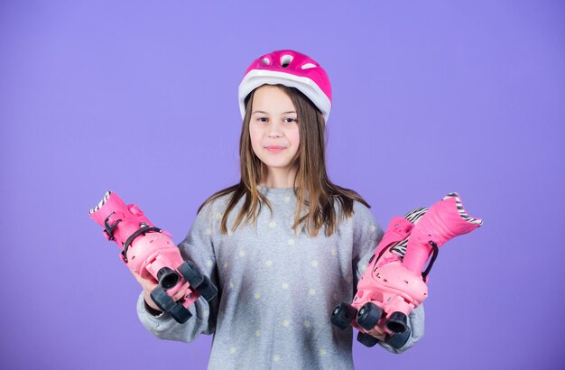 Meisje schattige tiener draagt helm en rolschaatsen op violette achtergrond Actieve vrije tijd en levensstijl Rolschaatsen tiener hobby Vrolijke tiener gaat rijden Sportief tienermeisje Klaar om te rolschaatsen