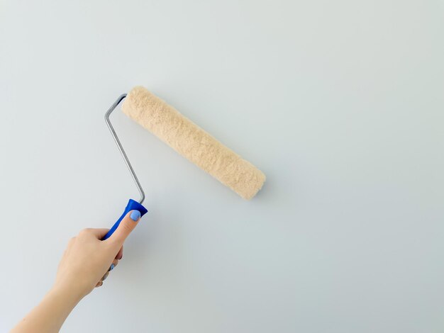 Meisje schildert de muur met witte verf vrouwelijke hand met muurverfroller close-up met kopieerruimte