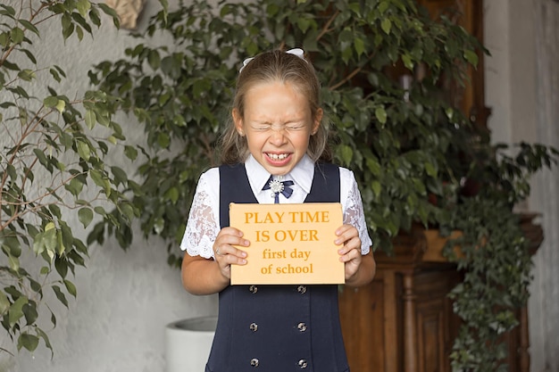 Meisje schoolmeisje met een boek met de inscriptie - speeltijd is voorbij, eerste schooldag.