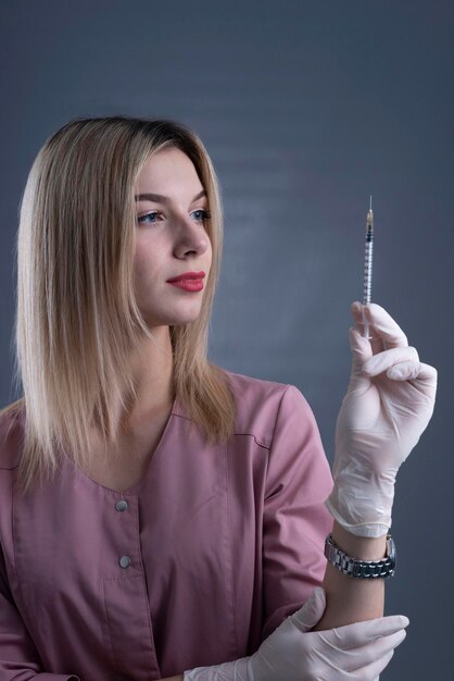 Meisje schoonheidsspecialiste houdt een spuit in haar hand op een grijze achtergrond