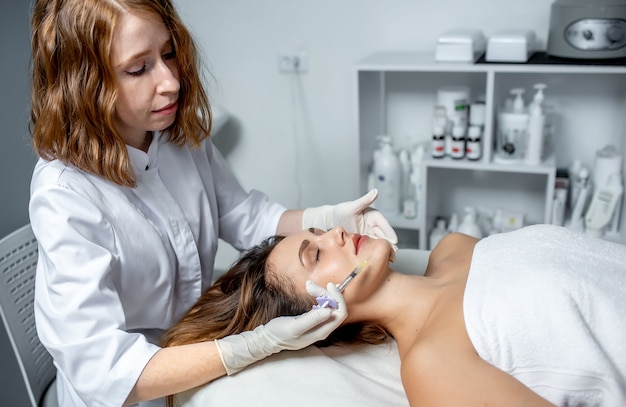 Meisje schoonheidsspecialiste maakt injecties op de lippen en het gezicht van een mooie vrouw in een cosmetische wig