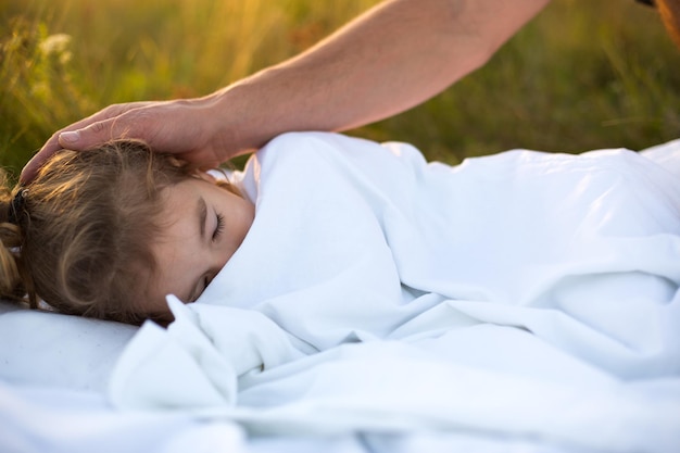 Meisje slaapt op wit bed in het gras frisse lucht Papa's hand klopt zachtjes op zijn hoofd Zorgbescherming Internationale kinderdag muggenbeten