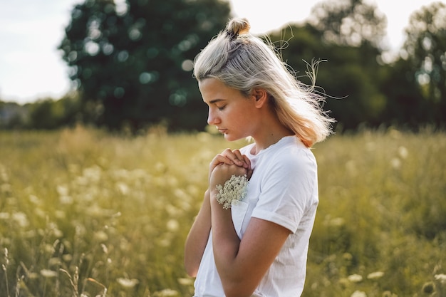 Meisje sloot haar ogen en bad in een veld. Handen gevouwen in gebed concept voor geloof