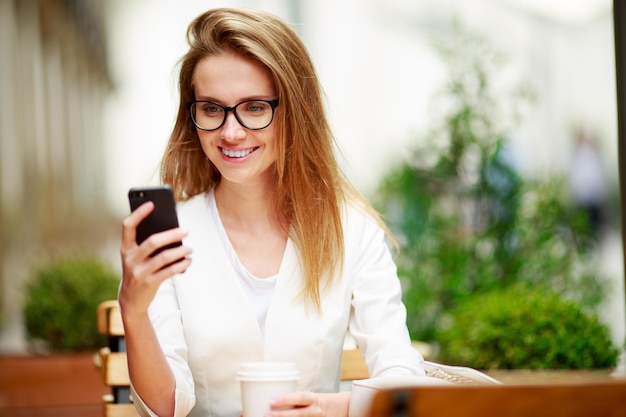 Meisje sms't op de smartphone op het terras van een restaurant met een ongerichte achtergrond