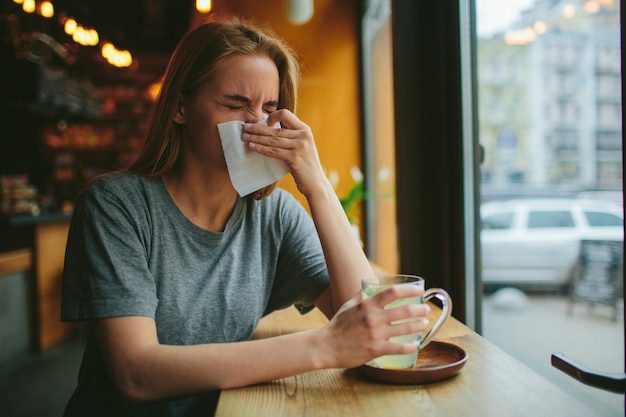 Meisje snuit haar neus in een café en drinkt thee. Ze heeft een loopneus.