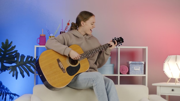 Meisje speelt akoestische gitaar thuis Grappige jonge vrouw speelt muziekinstrument op de bank