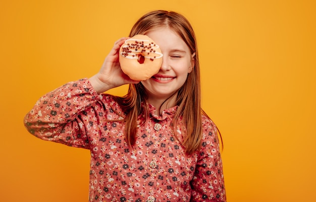 Meisje speelt en houdt donut vast als een bril dicht bij de ogen geïsoleerd op gele achtergrond