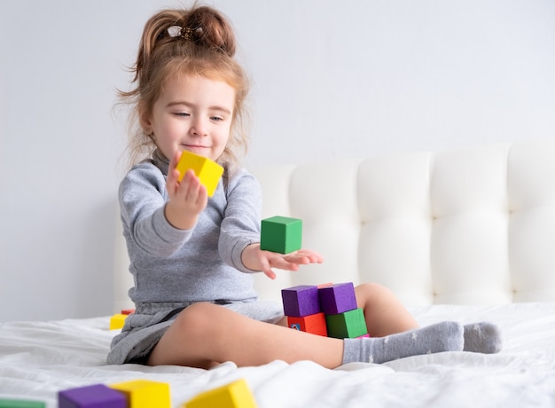 Meisje speelt met kleurrijke houten kubussen zittend op bed.