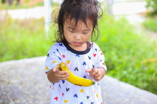 meisje speelt met teddybeer onder de boom en het eten van banaan