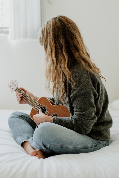 Foto meisje speelt ukelele op haar bed tijdens quarantaine