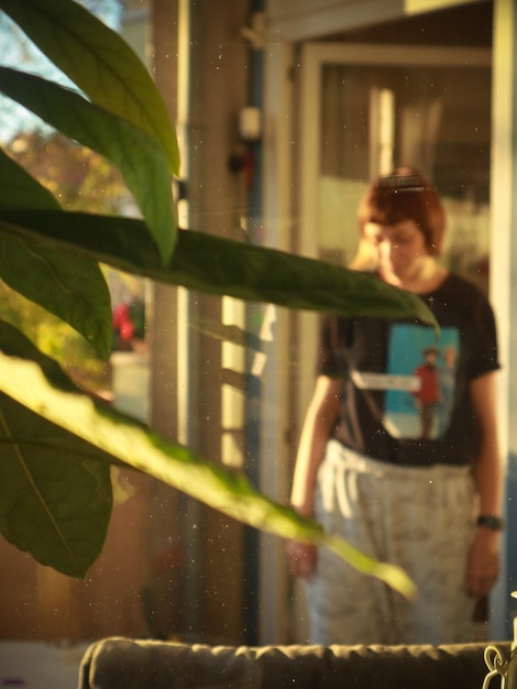 Foto meisje staat achter het raam in avocado bladeren en zonneschijn op het balkon