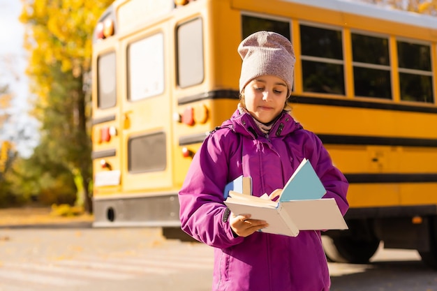 Meisje staat bij een grote schoolbus met haar boeken.