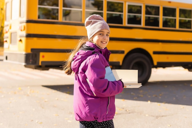 Meisje staat bij een grote schoolbus met haar boeken.