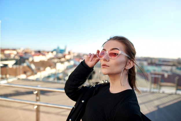 meisje staat bij het glazen hek en glas wordt gezien de stad, in roze zonnebril.