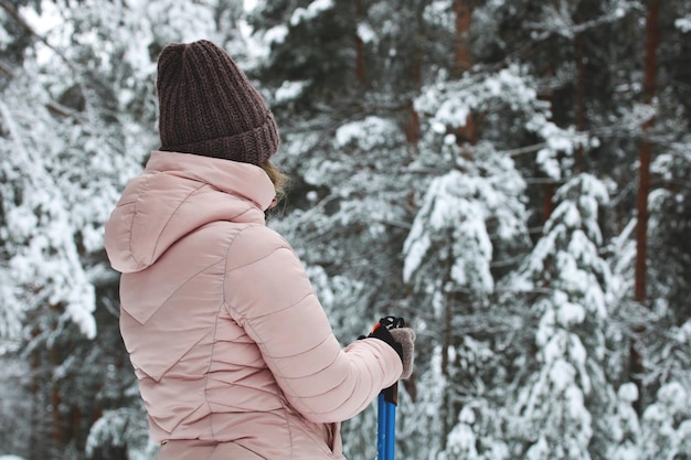 Meisje staat in een winterbos met stokken om te skiën of nordic walking