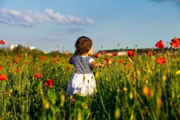 Meisje staat met uitgestrekte armen in het klaprozenveld en geniet van de natuur