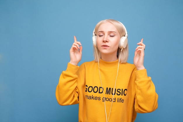 Meisje staat op blauw in de koptelefoon en luistert naar muziek met haar ogen dicht