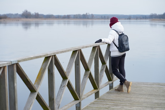 Meisje staat op een pier van winter meer en observeert landschap