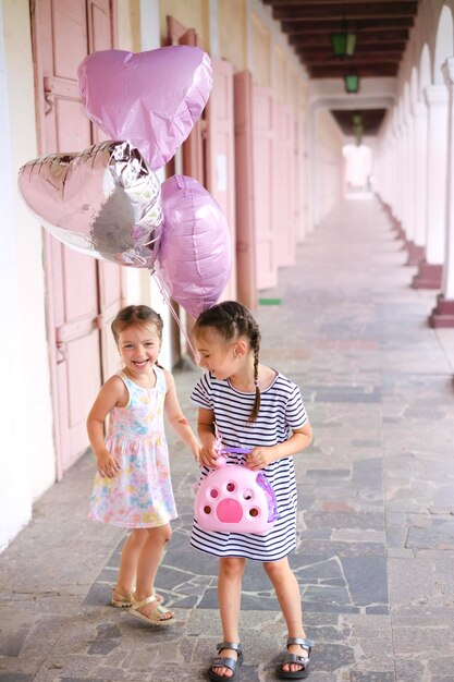 Meisje staat tussen de kolommen van een open stadsgebouw en houdt ballonnen vast