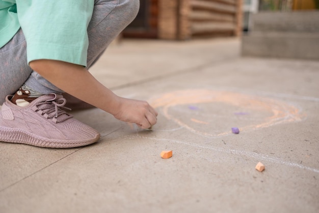Meisje tekent met kleurrijke kleurpotloden op de stoep Kindertekeningen met krijt op de muur Creatief kind Vreugde van de kindertijd