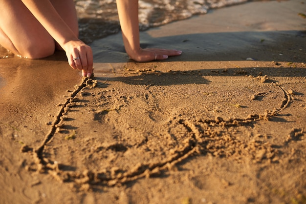 meisje tekent 's avonds met de vingers een hart op het zand bij de zee