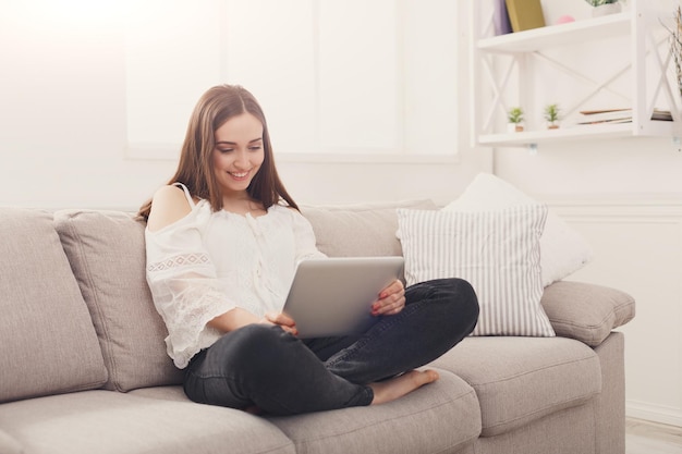 Meisje thuis surfen op het internet op tablet op beige bank in lichte woonkamer