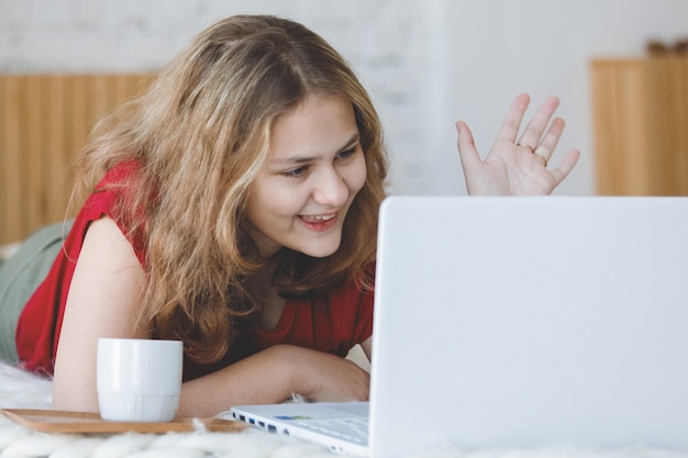 Meisje tiener blonde met een laptop ligt in bed op afstandsonderwijs