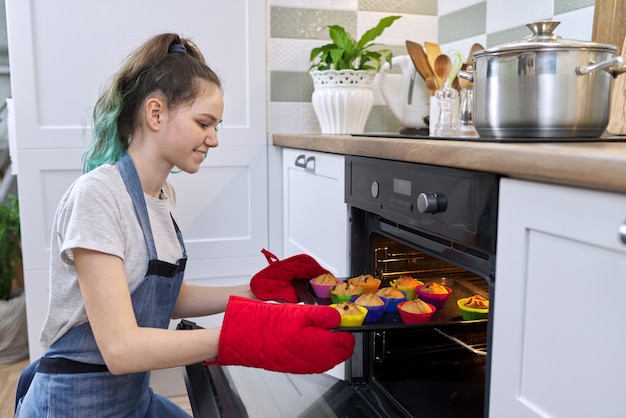 Meisje tiener food blogger koken Amerikaanse cupcakes. Meisje dat cake met hete versgebakken muffins uit de oven neemt