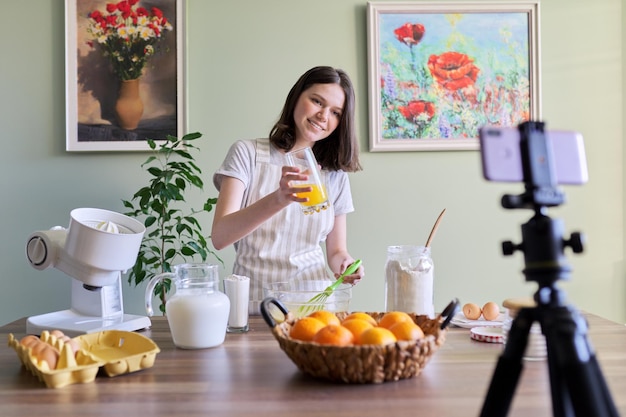 Meisje tiener food blogger opname recept voor het koken van oranje pannenkoeken. Vrouw thuis in de keuken, perst sap, glimlacht en kijkt naar camera, hobby en vrije tijd, gezond lekker zelfgemaakt voedselconcept