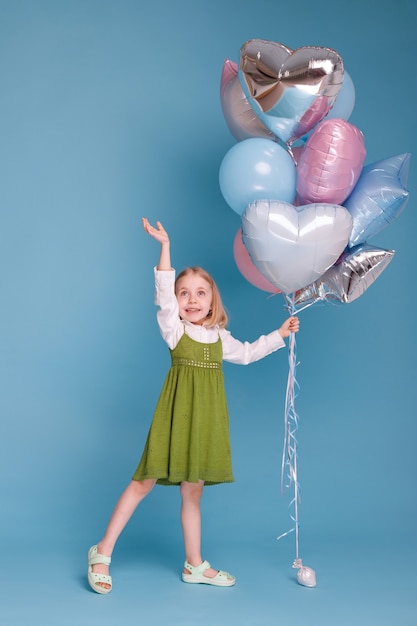 Meisje van 5 jaar oud in een groene jurk met ballonnen op een blauwe ondergrond