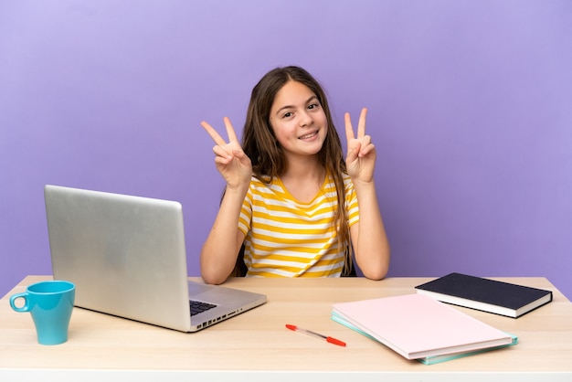 Meisje van de student op een werkplek met een laptop geïsoleerd op een paarse achtergrond met overwinningsteken met beide handen