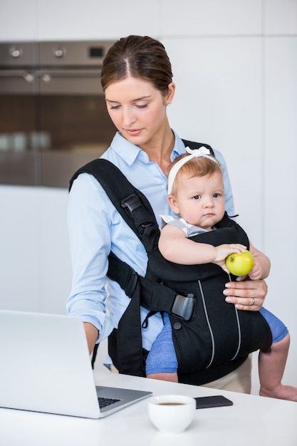 Meisje van de vrouwen het dragende baby terwijl het werken in laptop