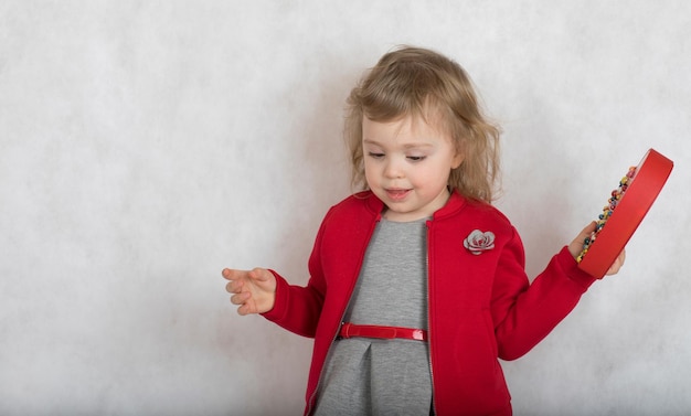 Meisje van twee jaar oud in rood grijs kostuum met een cadeautje op grijze achtergrond