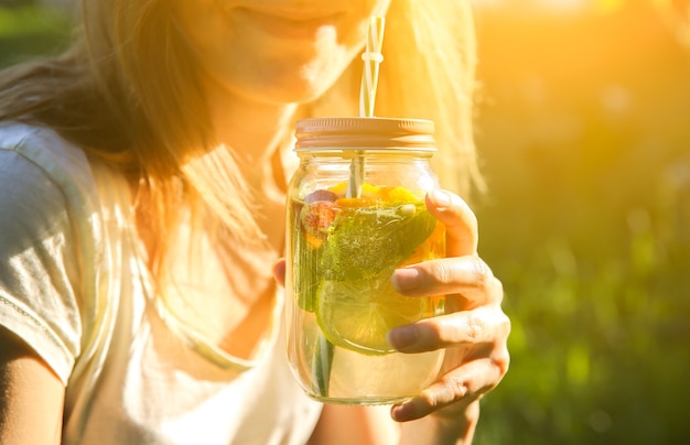 Foto meisje verse limonade drinken in potten met rietjes. hipster zomerdrankjes. milieuvriendelijk in de natuur. citroenen, sinaasappelen en bessen met munt in het glas.