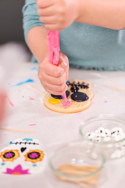 Meisje versieren suikerkoekjes met royal icing voor Dia de los Muertos vakantie.