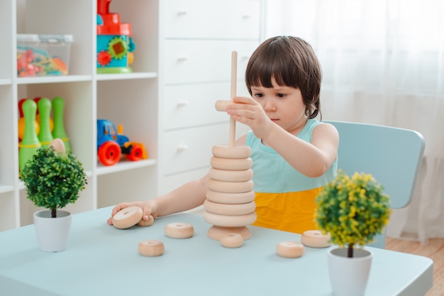 Meisje verzamelt een houten ongeverfde piramide. Veilig natuurlijk houten kinderspeelgoed.