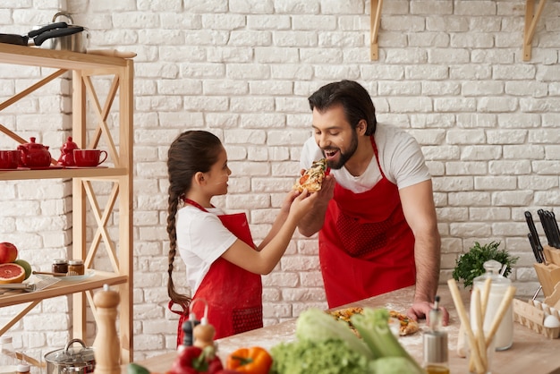 Meisje voedt hongerige vader met een stuk pizza.